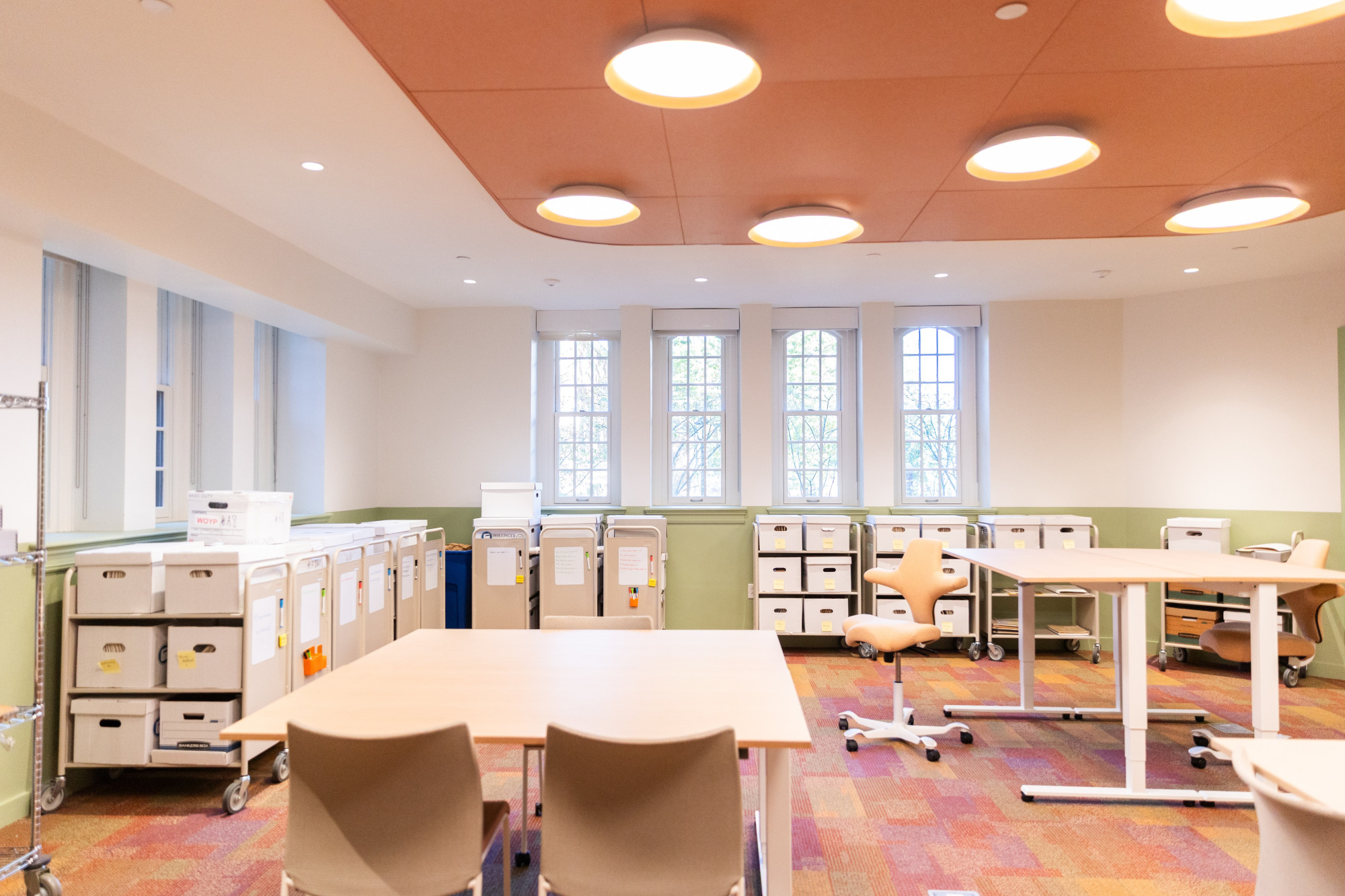 A brightly lit workshop space with movable tables and chairs and carts for archival files.