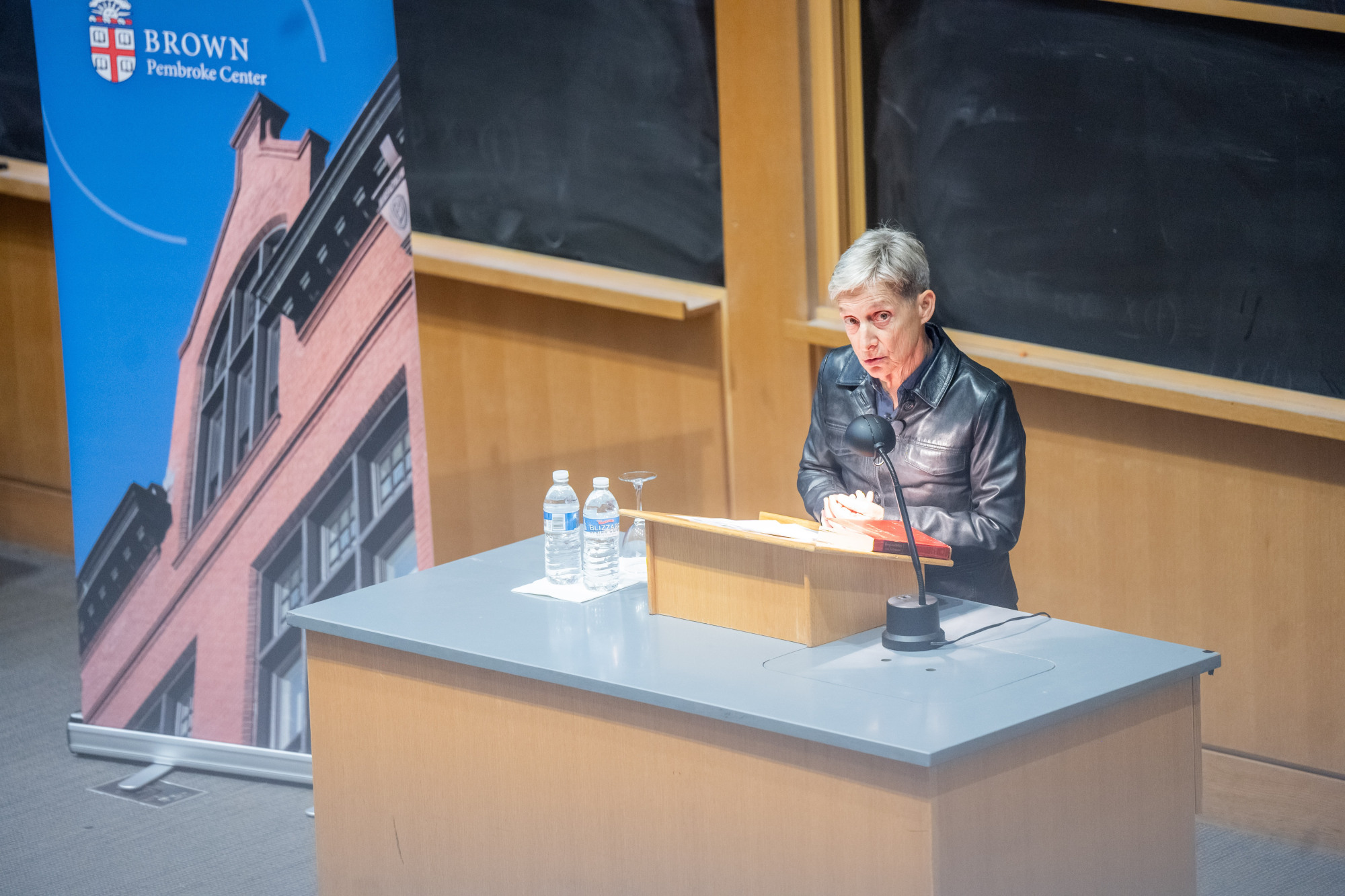Judith Butler stands at a lectern speaking into a microphone. 