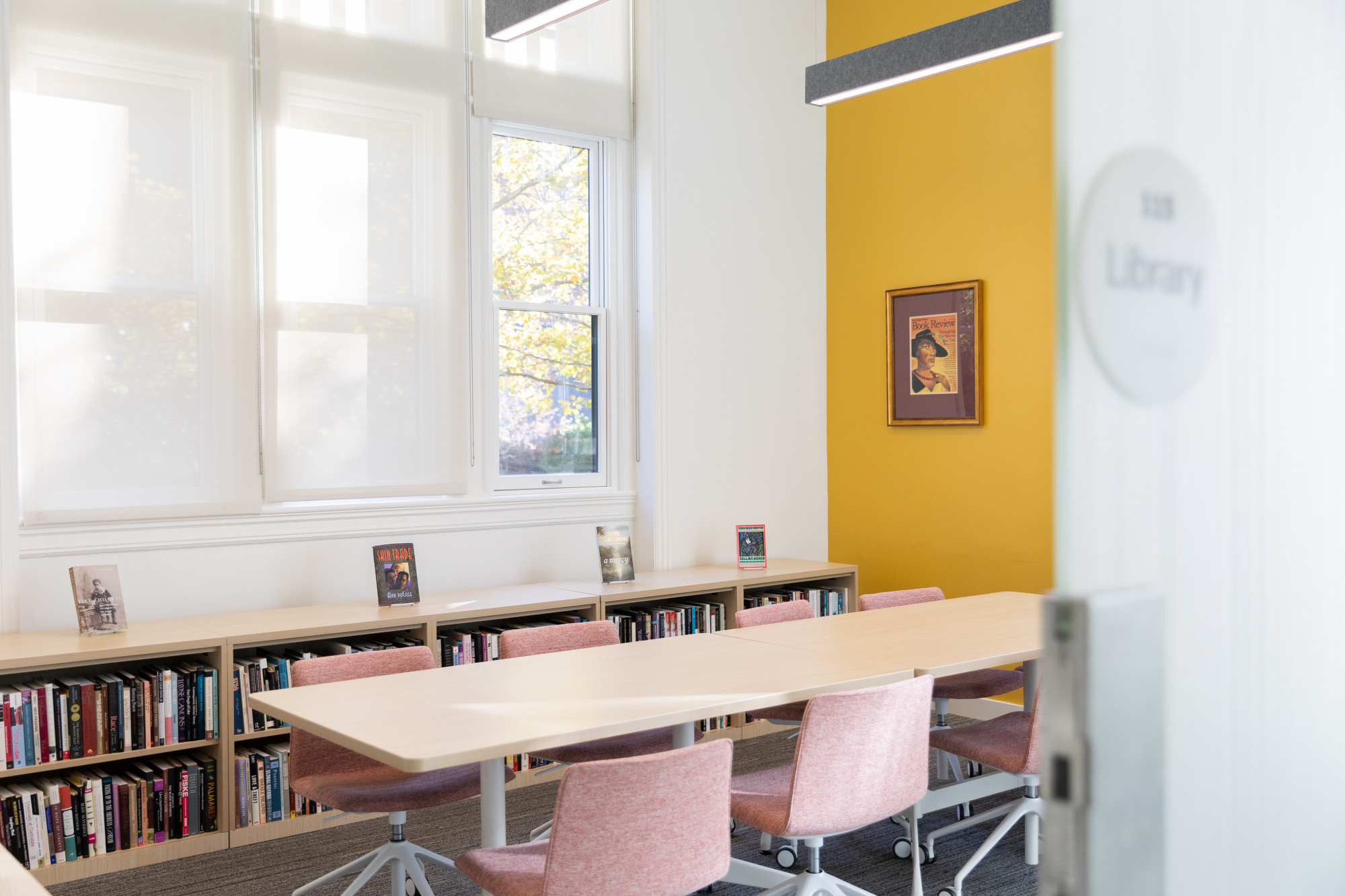 The Pembroke Hall library room, with windows, low bookshelves, and a conference table with chairs.