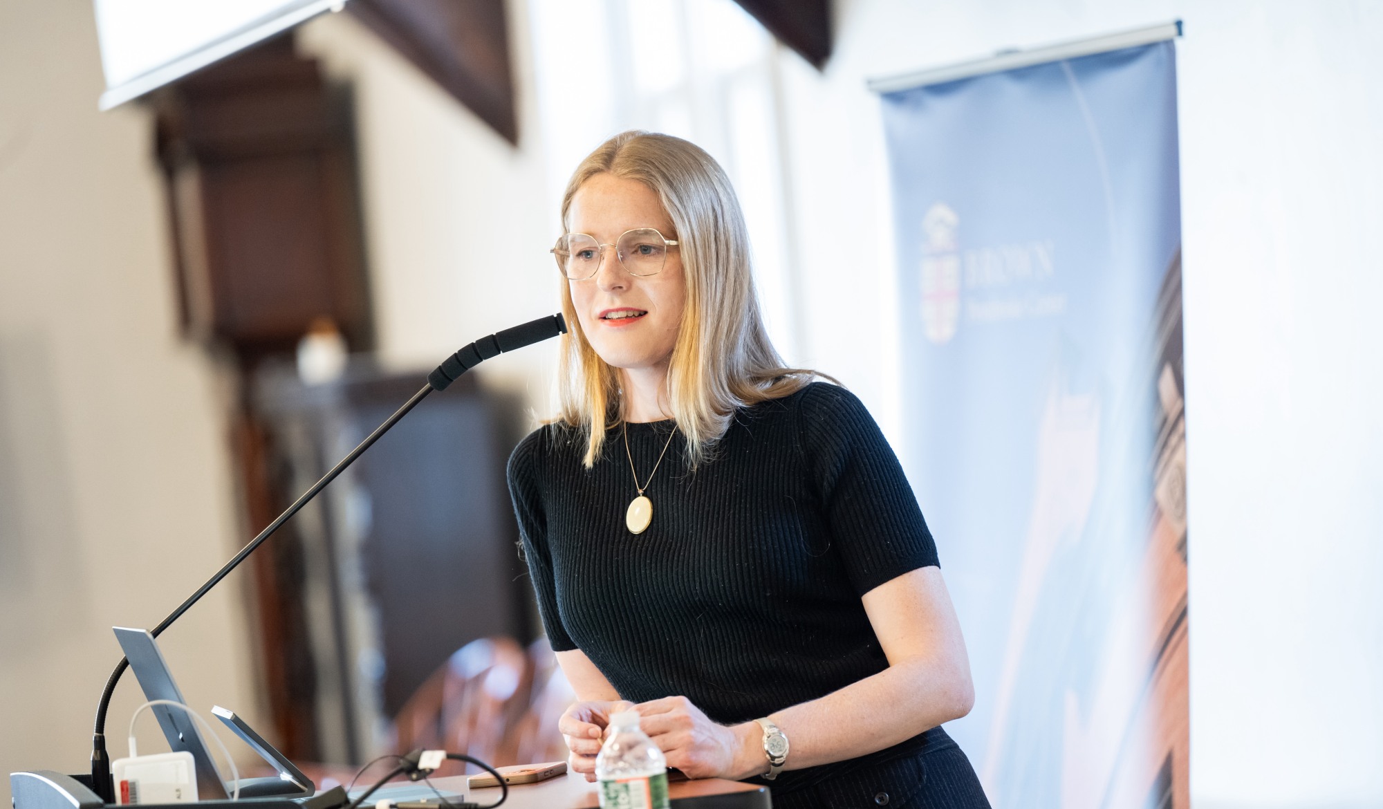 Gillian Branstetter leans against a lectern and speaks into a microphone.