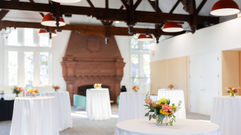 The updated room 305 with a fireplace on the far wall, tables with tablecloths and flowers in the middle. The room is bright and filled with light.