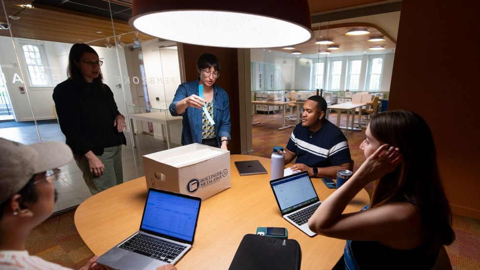 Archivists stand in front of boxes on a circular table. Three students are seated around the table, with laptops open.