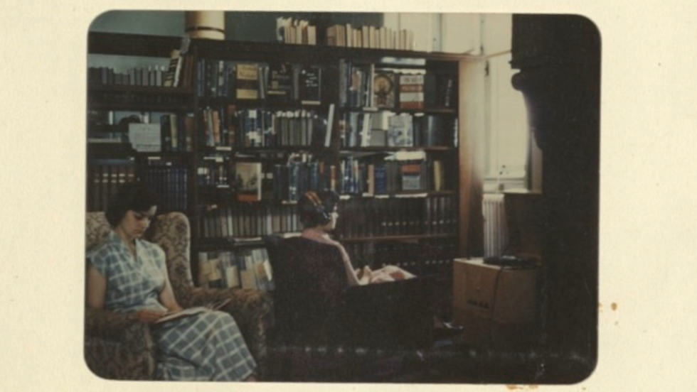 An older color photograph shows two Pembroke College students sitting in armchairs in the library. One is listening to a record player on headphones.